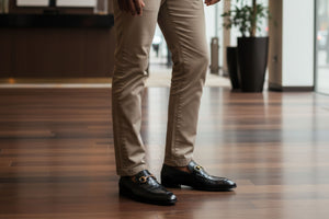 Close-up of a person wearing beige pants and green dress shoes on a wooden floor.