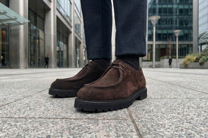 C Collection Brown suede shoes worn by a person standing on a city street.
