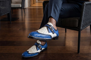 Man sitting in chair dressed in all black with blue and white exotic shoes on