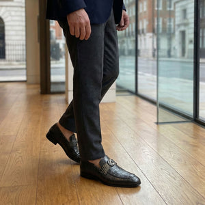 Person wearing dark trousers and patterned shoes on a wooden floor.