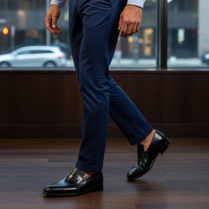 Person wearing navy blue pants and black shoes on a wooden floor.