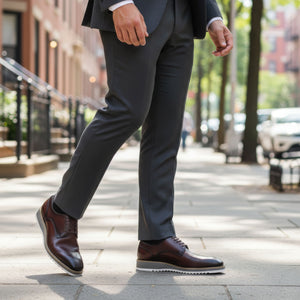 Person wearing a dark suit and brown shoes on a city street.