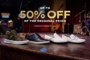 Four styles of casual shoes lined up on a wooden stage: a camouflage sneaker, a black leather oxford, a white woven slip-on, and a white leather loafer. Large promotional text reads 'UP TO 50% OFF OF THE ORIGINAL PRICE' over a dark concert-stage background.