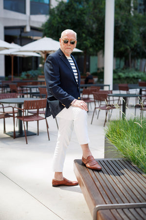 Man in sunglasses and a dark jacket sitting on a bench outdoors.